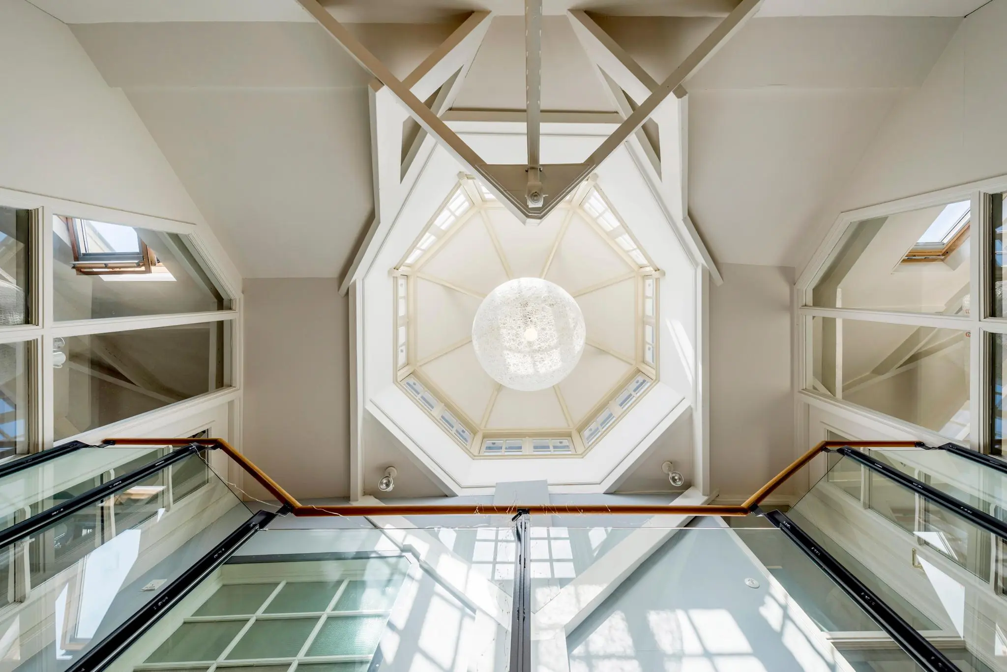 Glazen trapopgang met zicht op een achthoekige lichtkoepel en moderne hanglamp in de Prof. Tulpstraat.